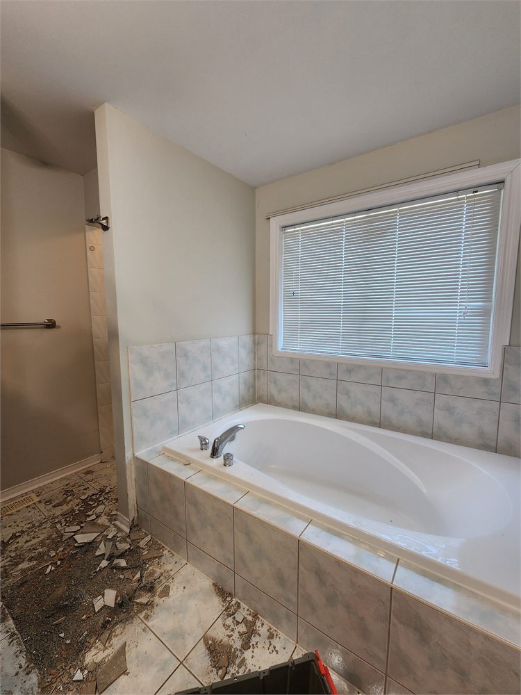 Old tiled tub deck and cracked floor tile during demolition, before the remodel