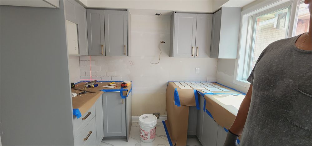 Subway tile backsplash being laid out against grey shaker cabinets